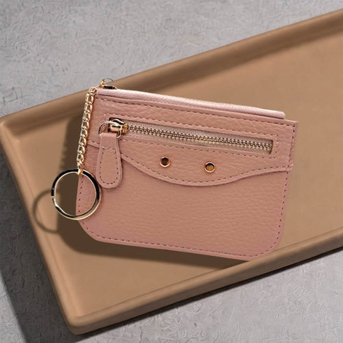Compact slim faux leather zip card holder with key ring in pink color resting on a neutral tray.